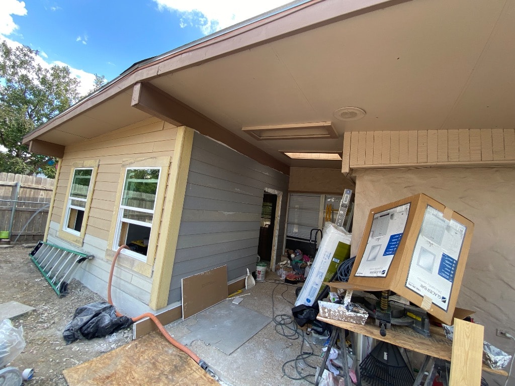 Home addition framing wrapped in Tyvek housewrap with window rough openings cut and lumber staged on site