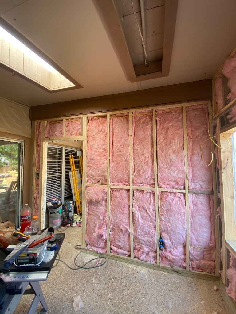 Interior of kitchen addition showing pink batt insulation in stud bays, electrical rough-in wiring, and skylight framing before drywall