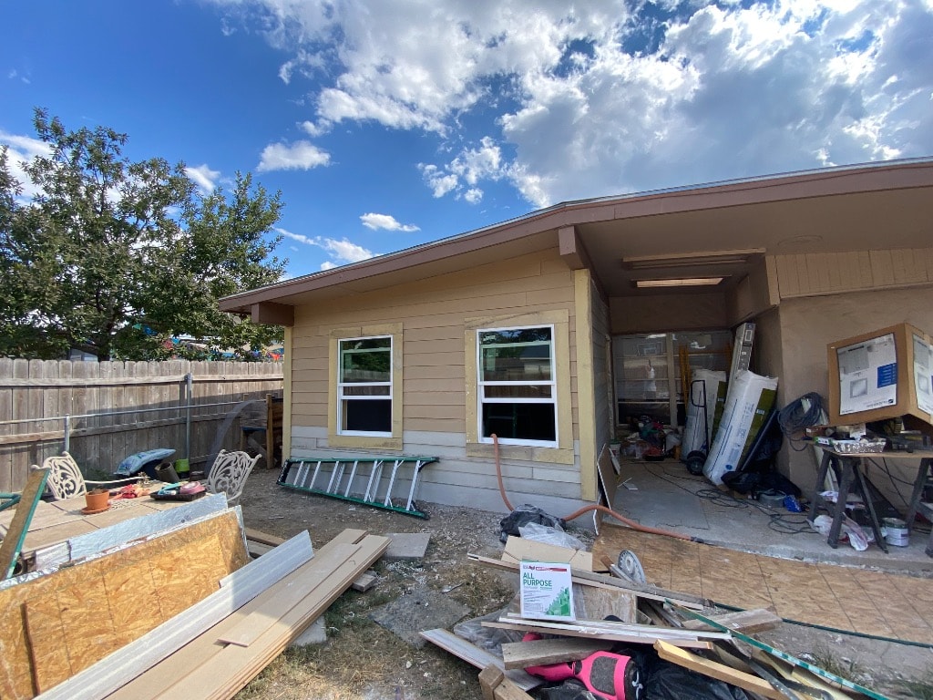 Home addition with new lap siding installed, windows and door set in openings, and new materials staged outside during construction