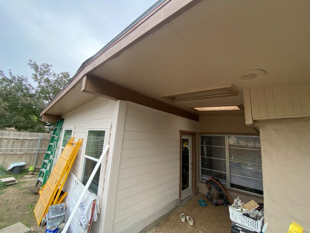 Wide exterior view of completed home addition showing new lap siding, double windows, roofline tied into existing structure, and construction materials on site