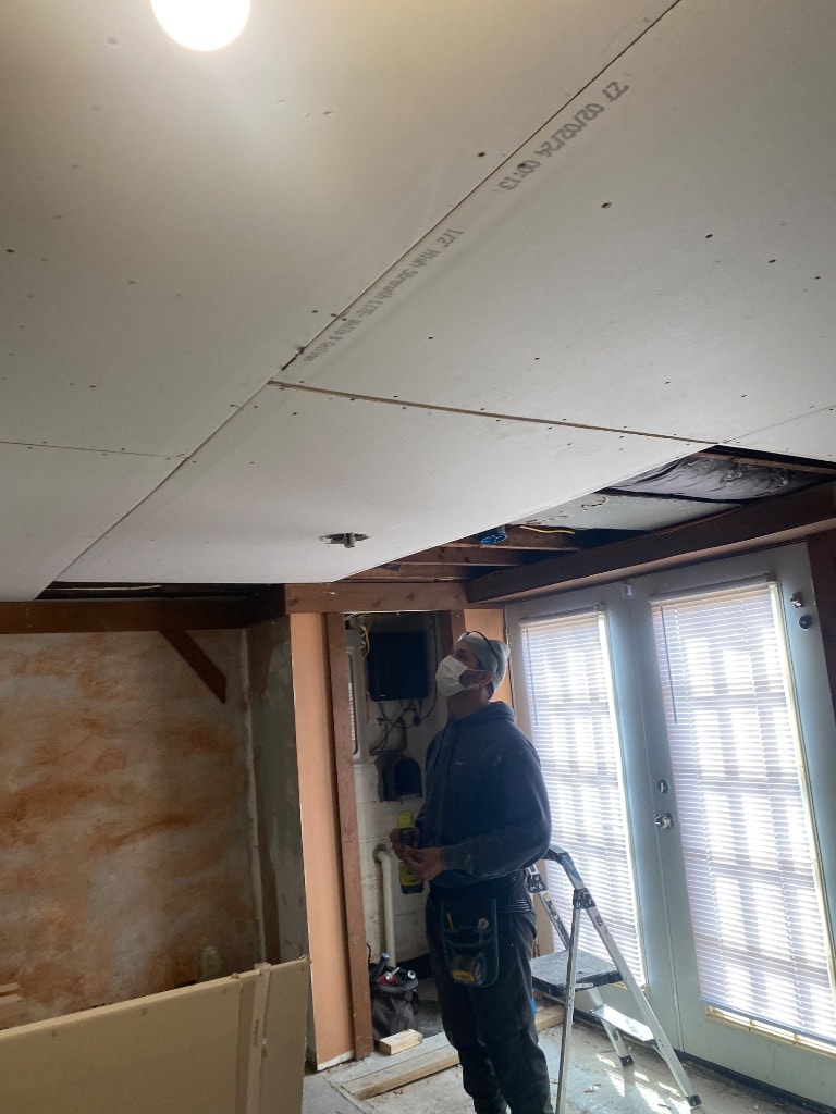 Contractor hanging drywall on basement ceiling with electrical rough-in visible and waterproofed walls in background