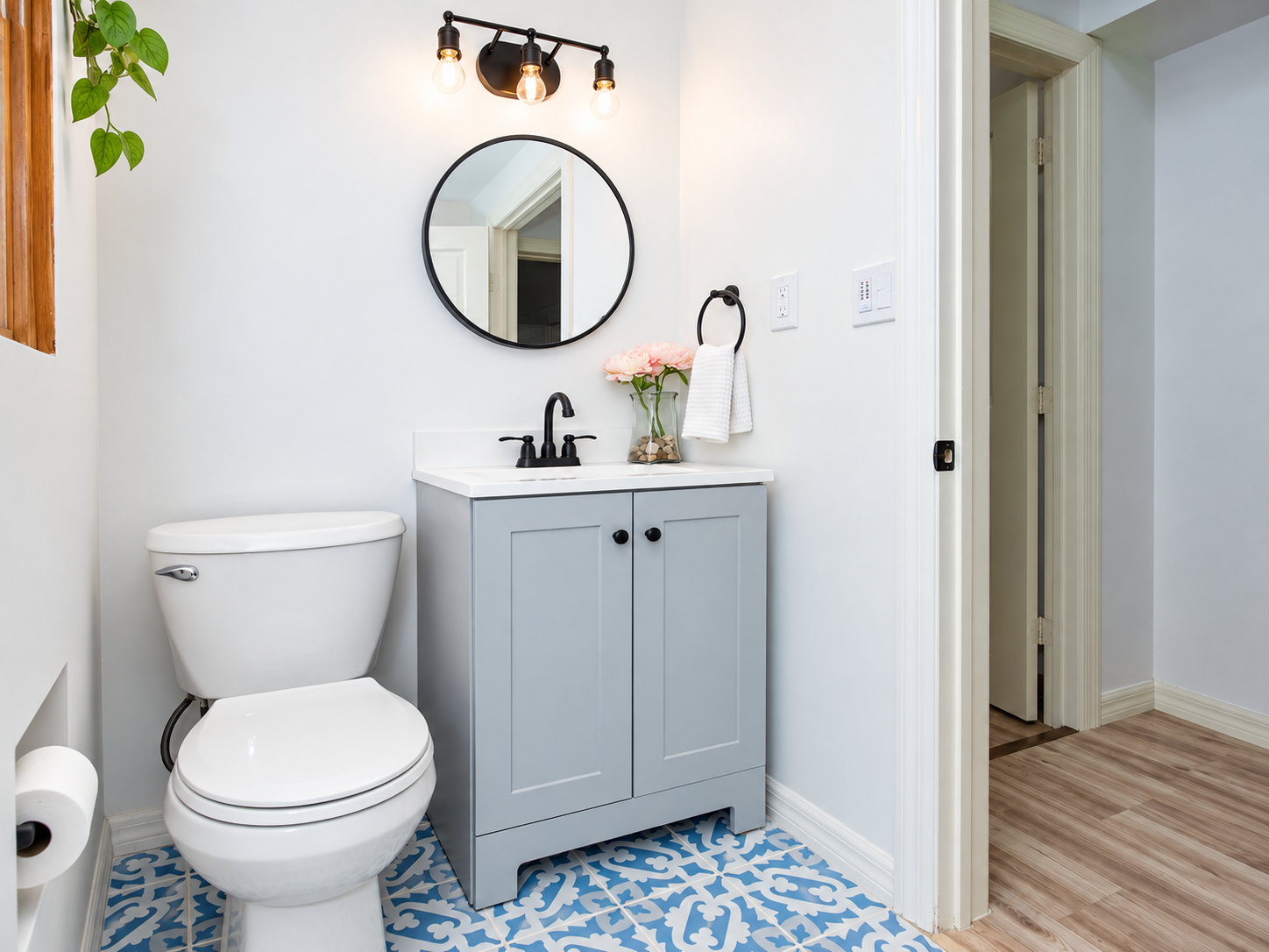 Finished bathroom with gray shaker vanity, round mirror, matte black fixtures, and blue patterned mosaic tile floor