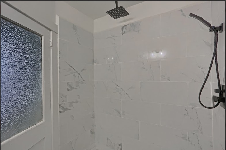 Completed marble tile shower enclosure with rainfall ceiling showerhead and matte black fixtures