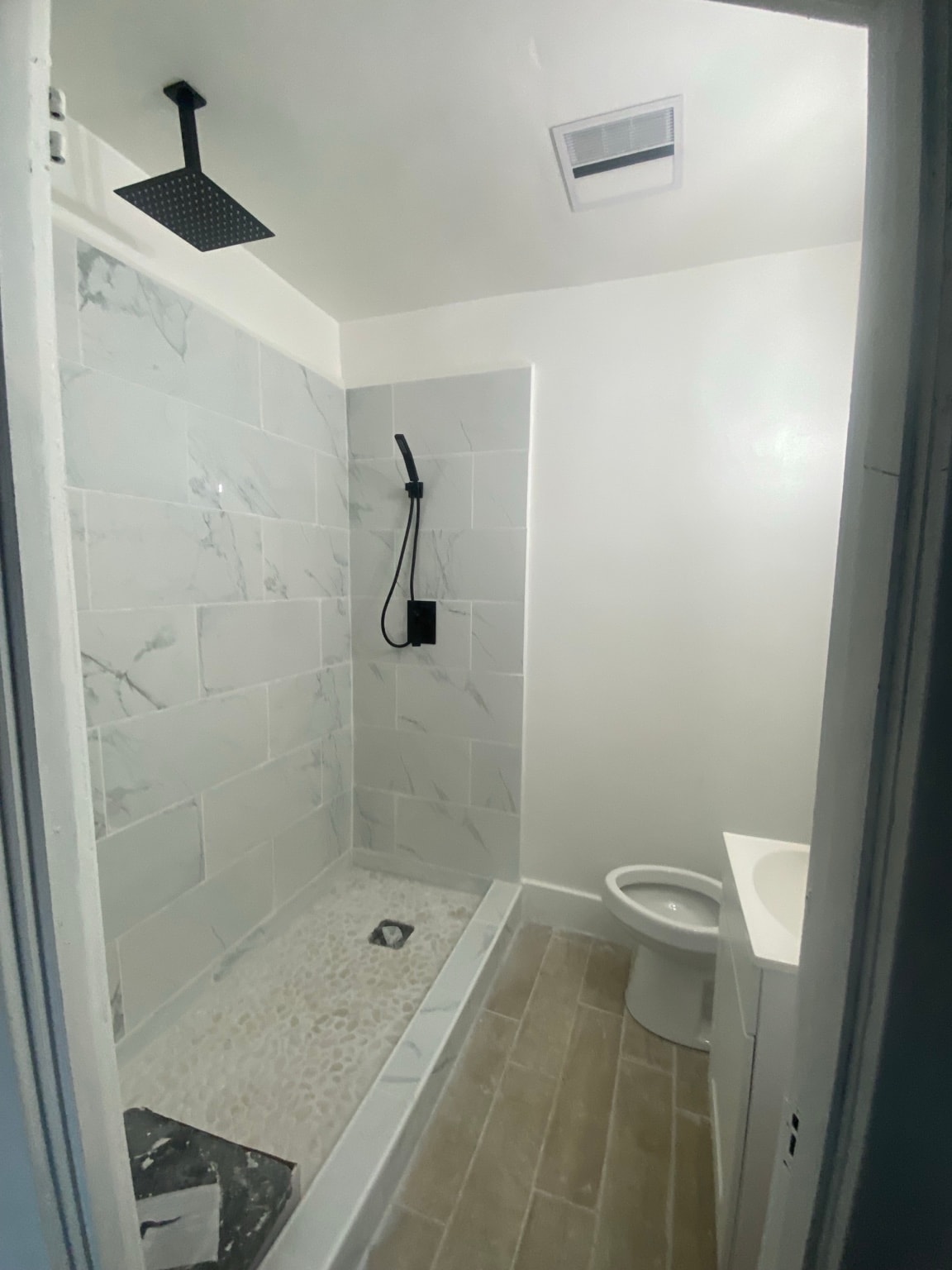 Bathroom renovation in progress showing marble tile shower installation with pebble floor and ceiling-mount showerhead rough-in