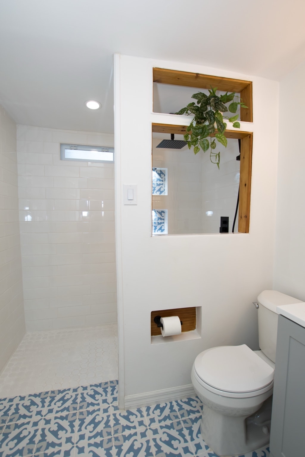 Completed open walk-in shower with white subway tile walls, blue patterned mosaic floor, and built-in wood shelf niches