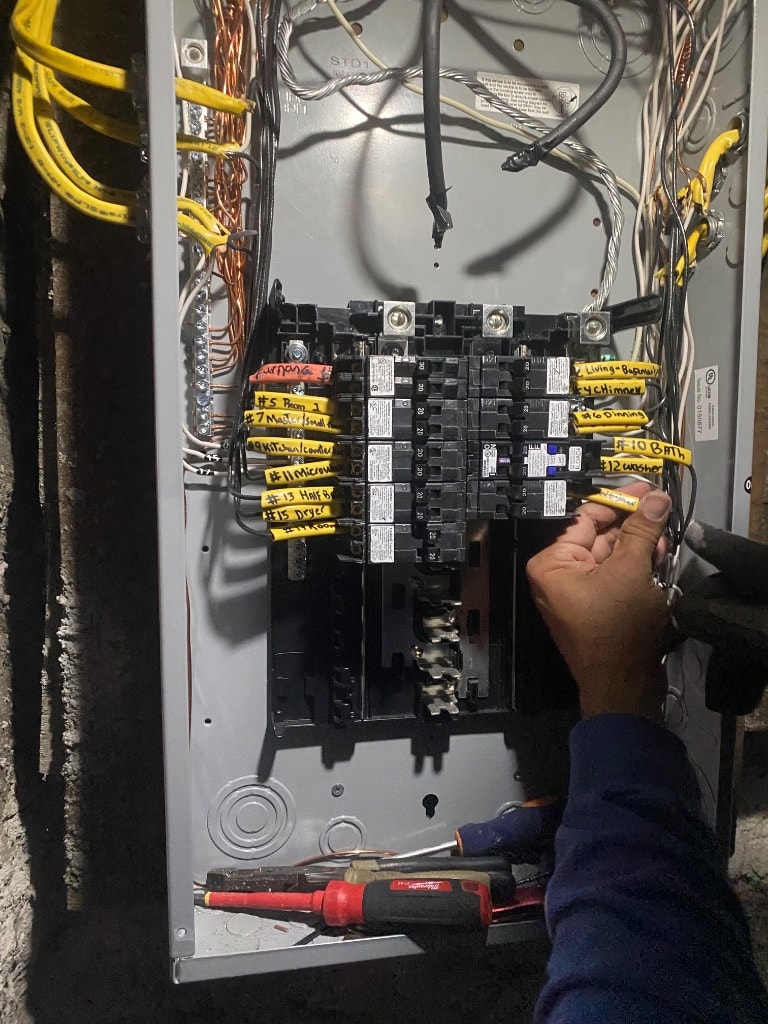Electrician wiring and labeling a residential electrical panel with new circuit breakers during home renovation