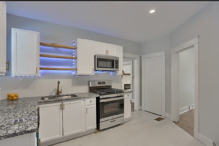 Full kitchen remodel showing white cabinetry, stainless appliances, granite counters, and porcelain tile flooring