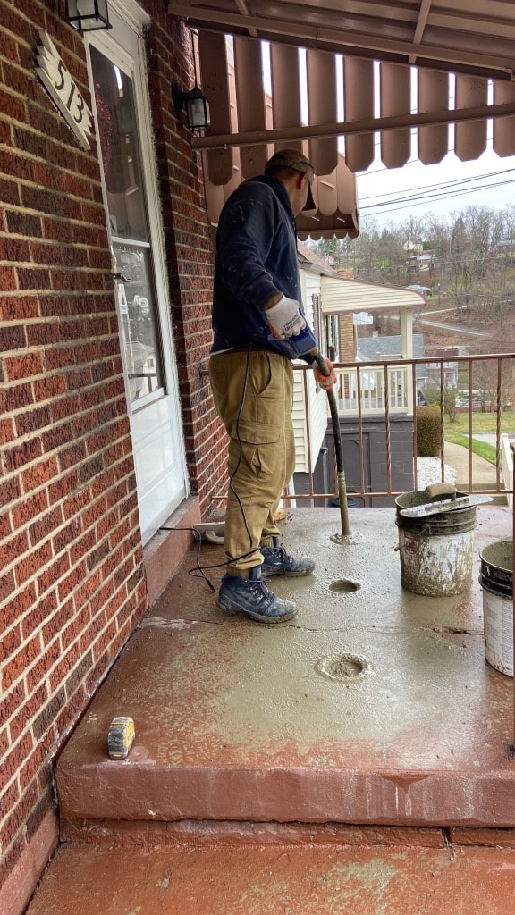 Worker vibrating and finishing fresh concrete on a brick home front porch during resurfacing project in Pittsburgh