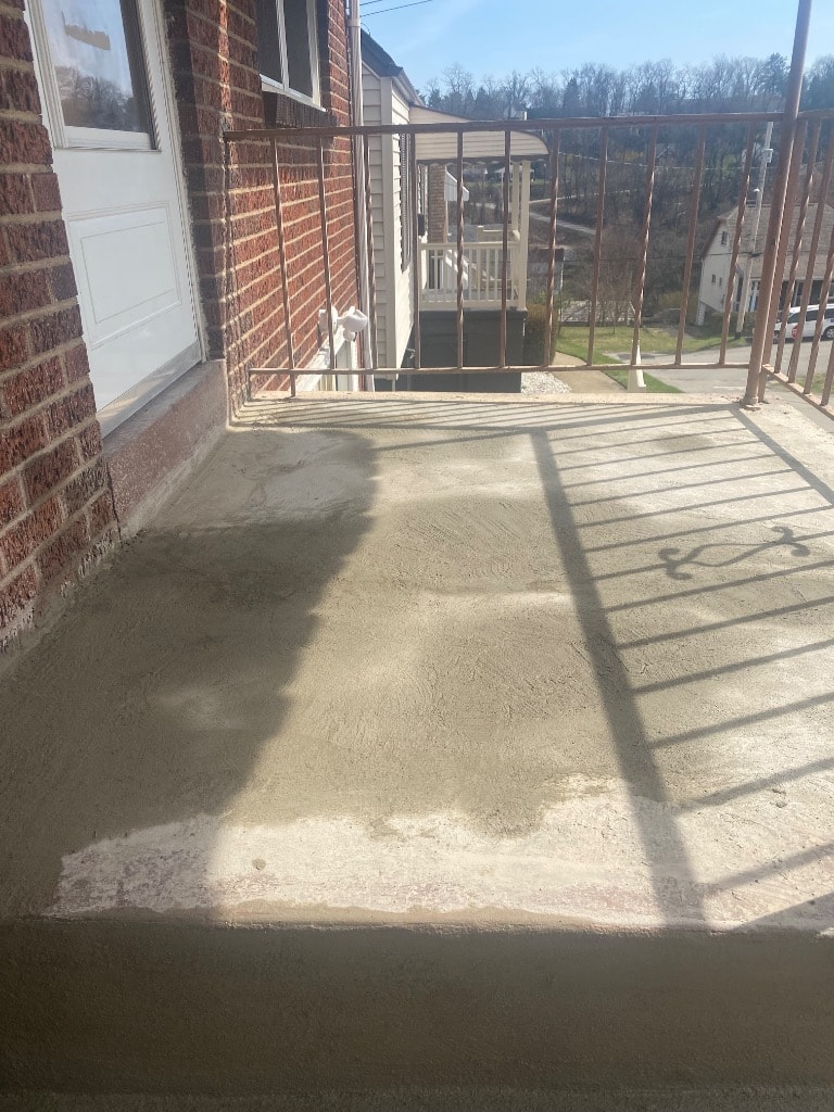 Freshly resurfaced concrete porch deck on a Pittsburgh brick home showing smooth new finish with trowel texture and metal railing