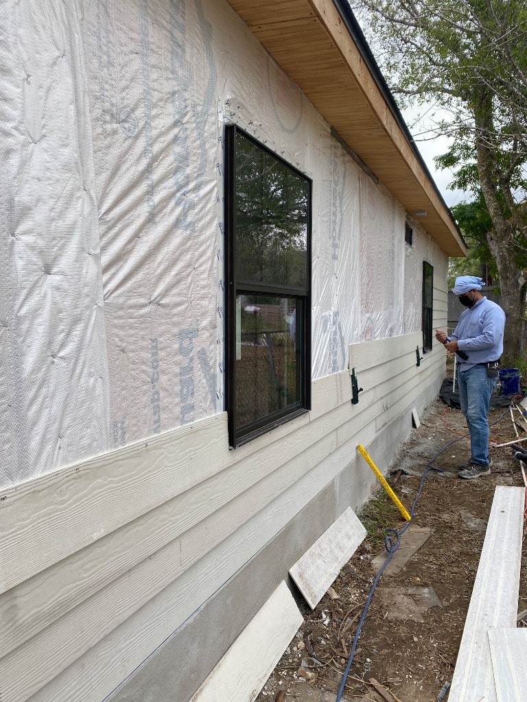 Set2 Go crew member installing gray lap siding with black windows set in openings, housewrap visible, and siding materials staged on site
