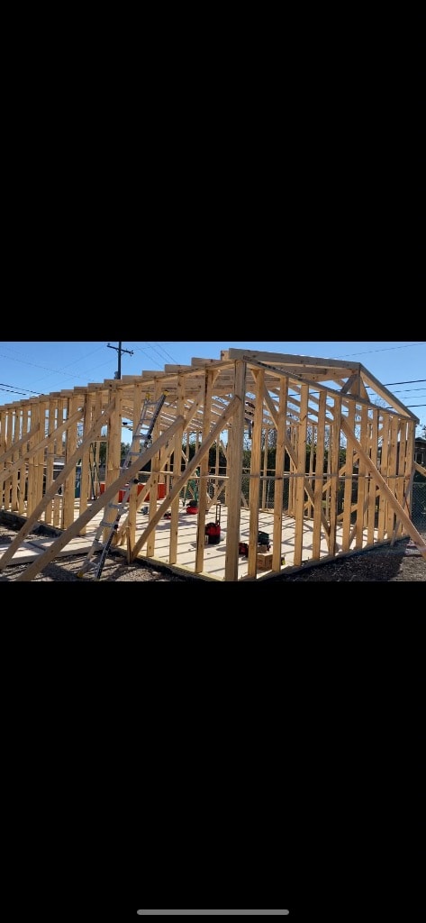 New structure build showing complete wood stud framing with roof trusses open to sky and tools staged on concrete slab